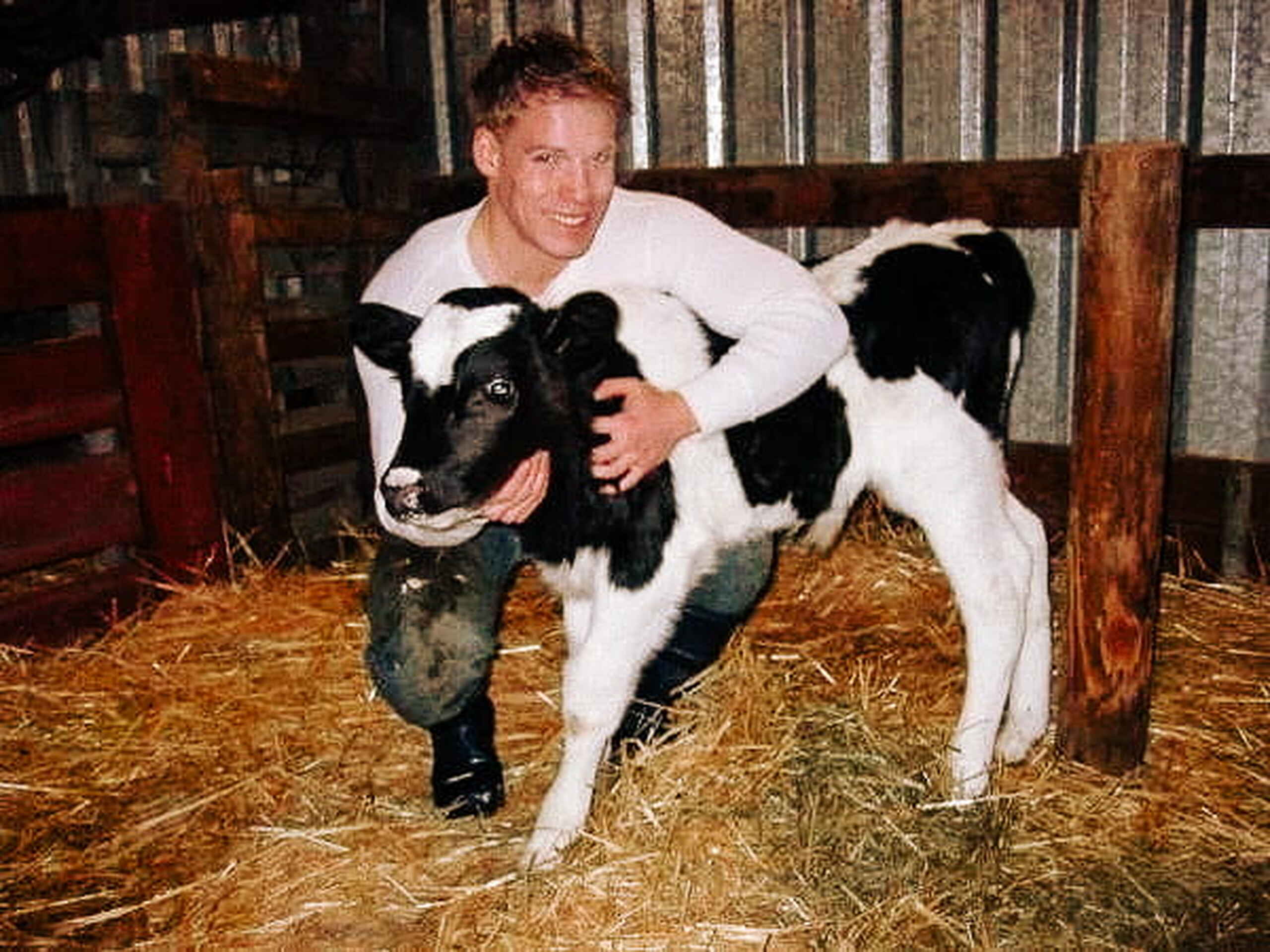 Man posing with a black and white dairy calf in a barn