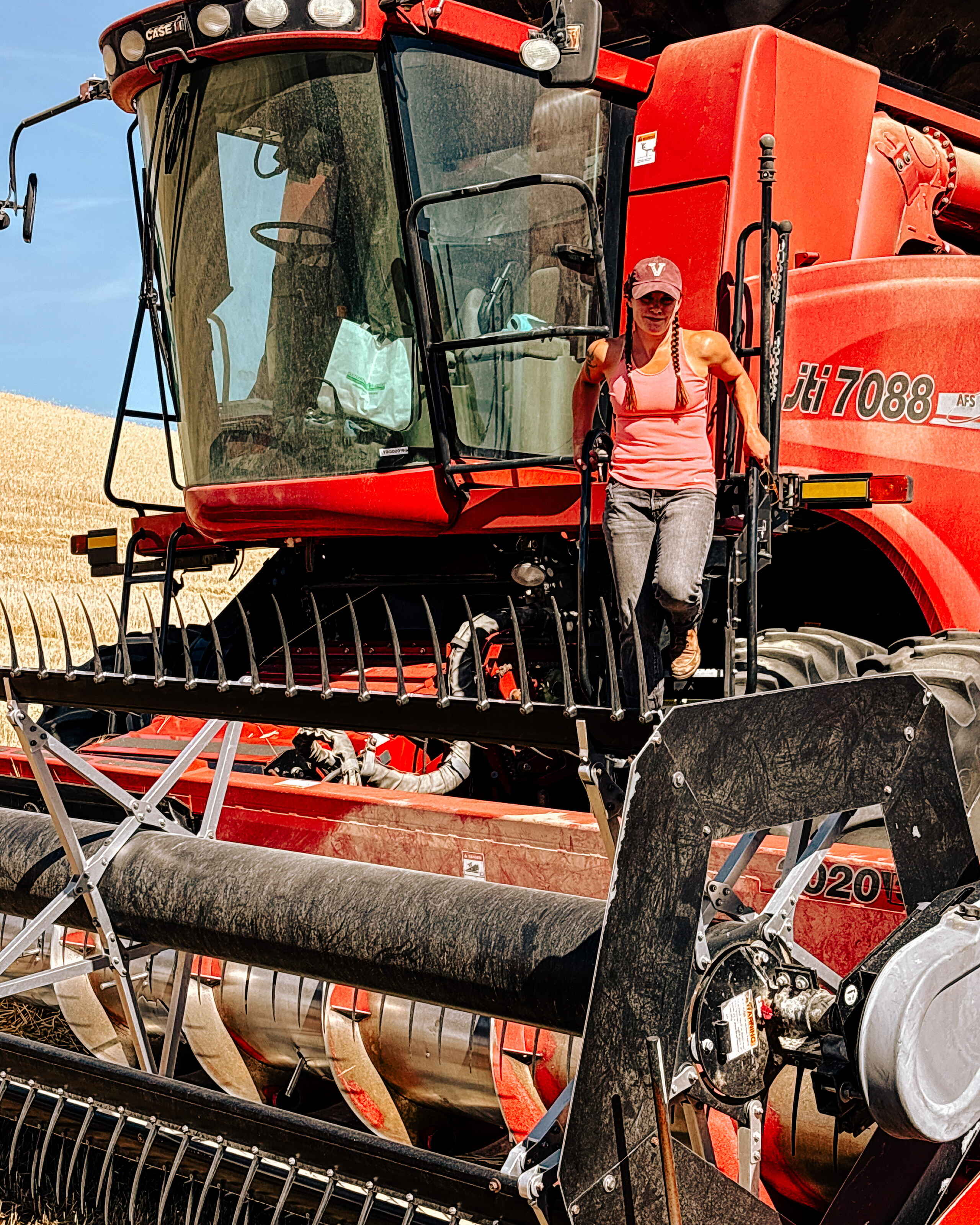 Woman standing on the step of a red Case IH combine harvester in a grain field