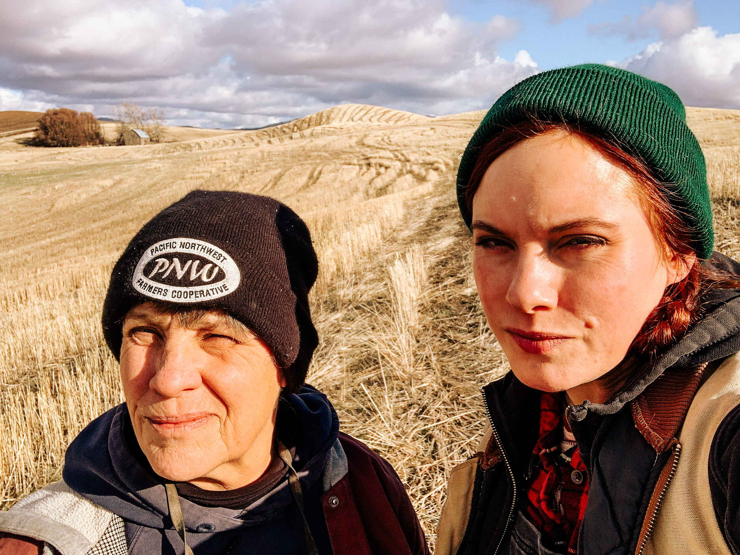Sheryl and Ariel Zakarison stand together in a harvested grain field under partly cloudy skies
