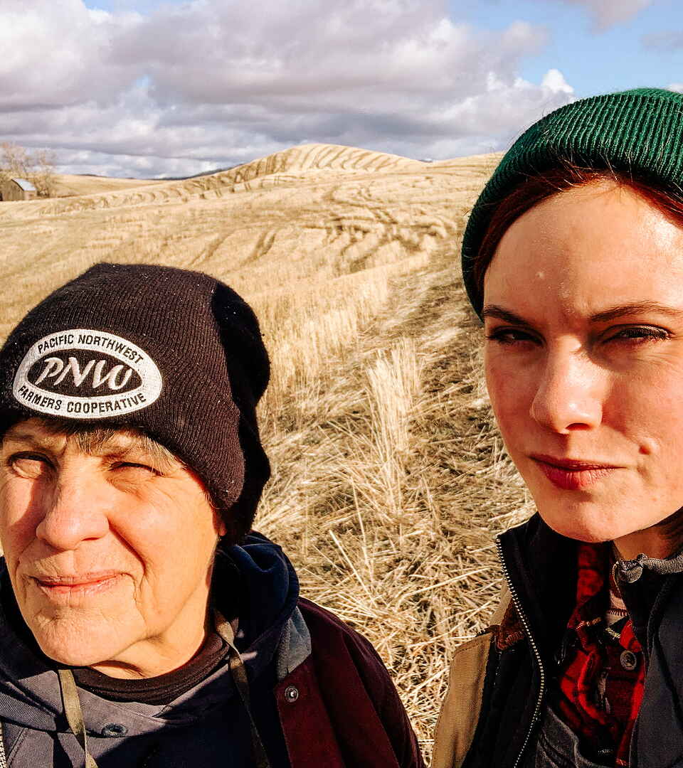 Sheryl and Ariel Zakarison stand together in a harvested grain field under partly cloudy skies