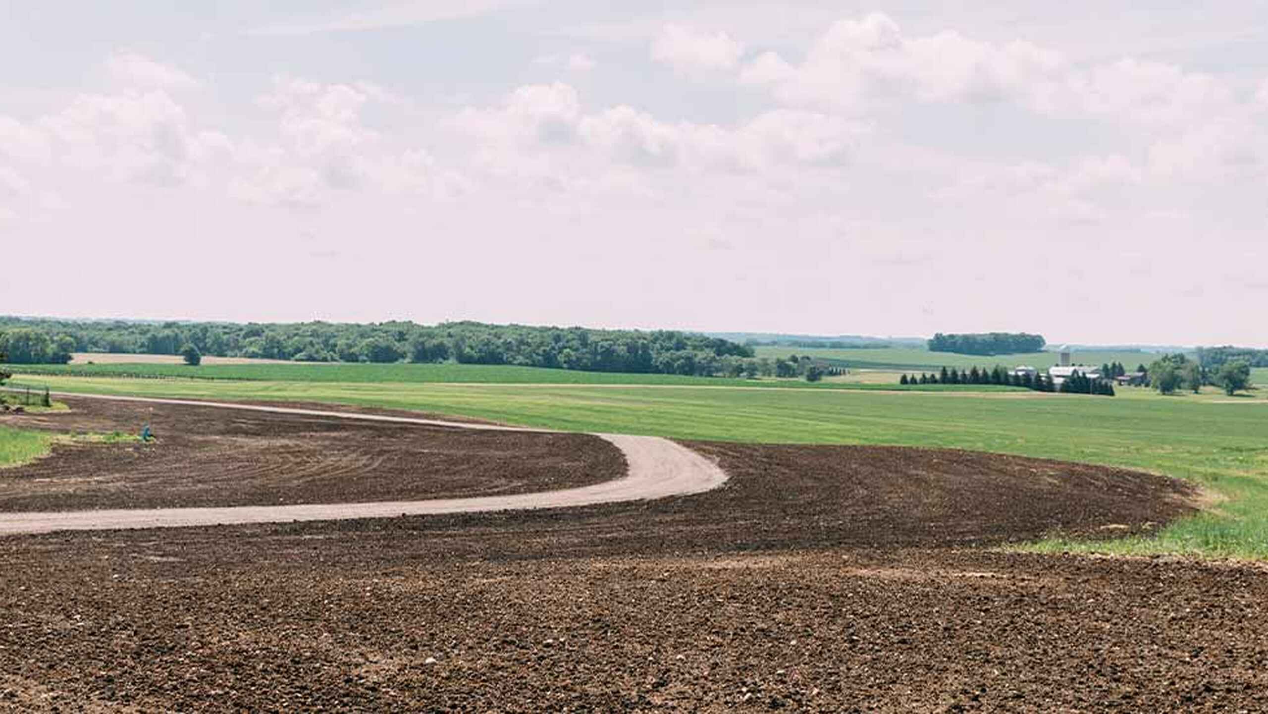 Curved contour farming pattern with plowed brown soil and green crop rows across rolling farmland
