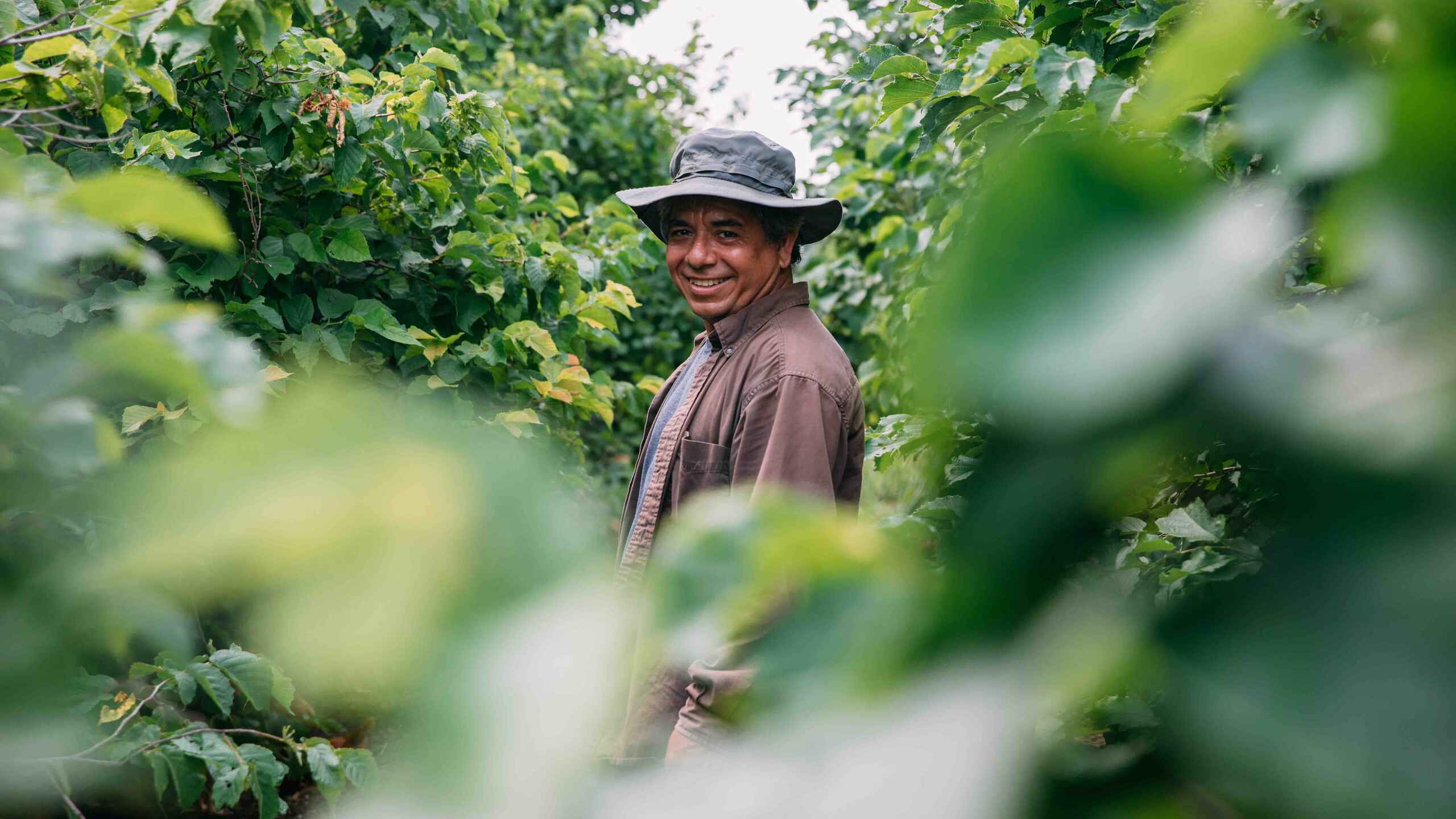 Farmer smiling at camera while standing in a leafy crop field