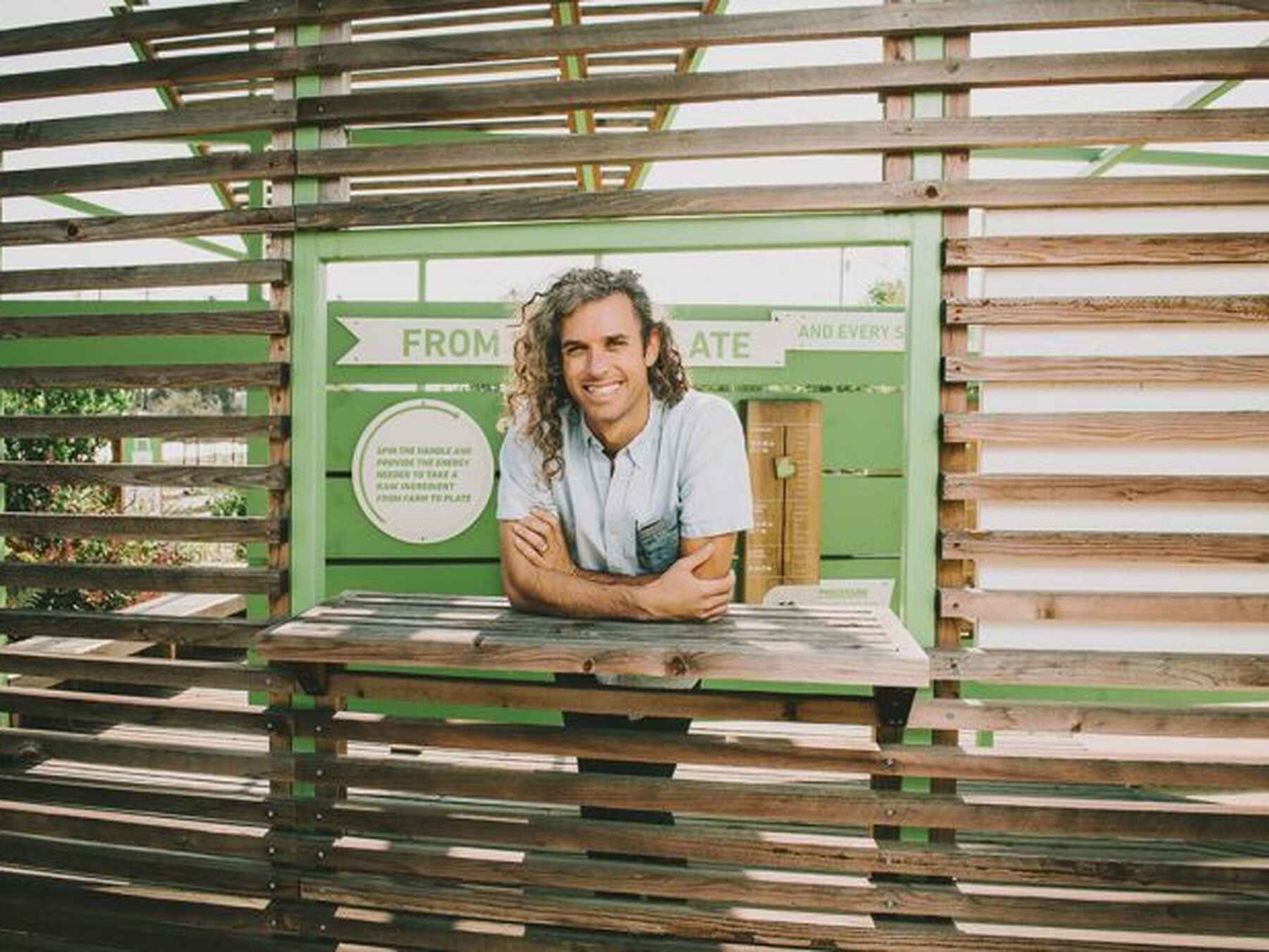Evan Marks stands at a wooden window opening with a green banner displaying his name and organization
