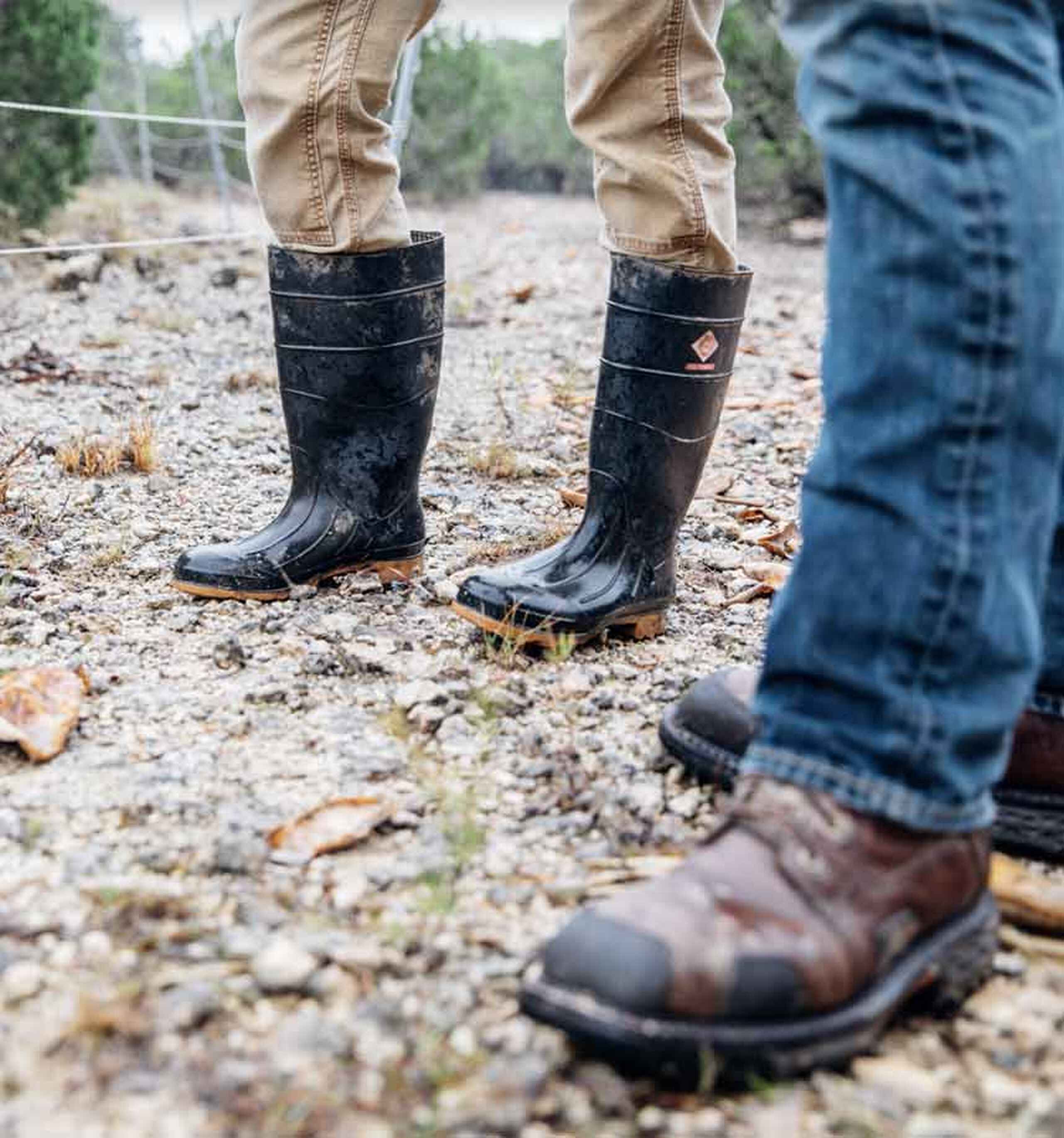 Three people wearing different types of footwear stand on gravel ground during an outdoor farm visit