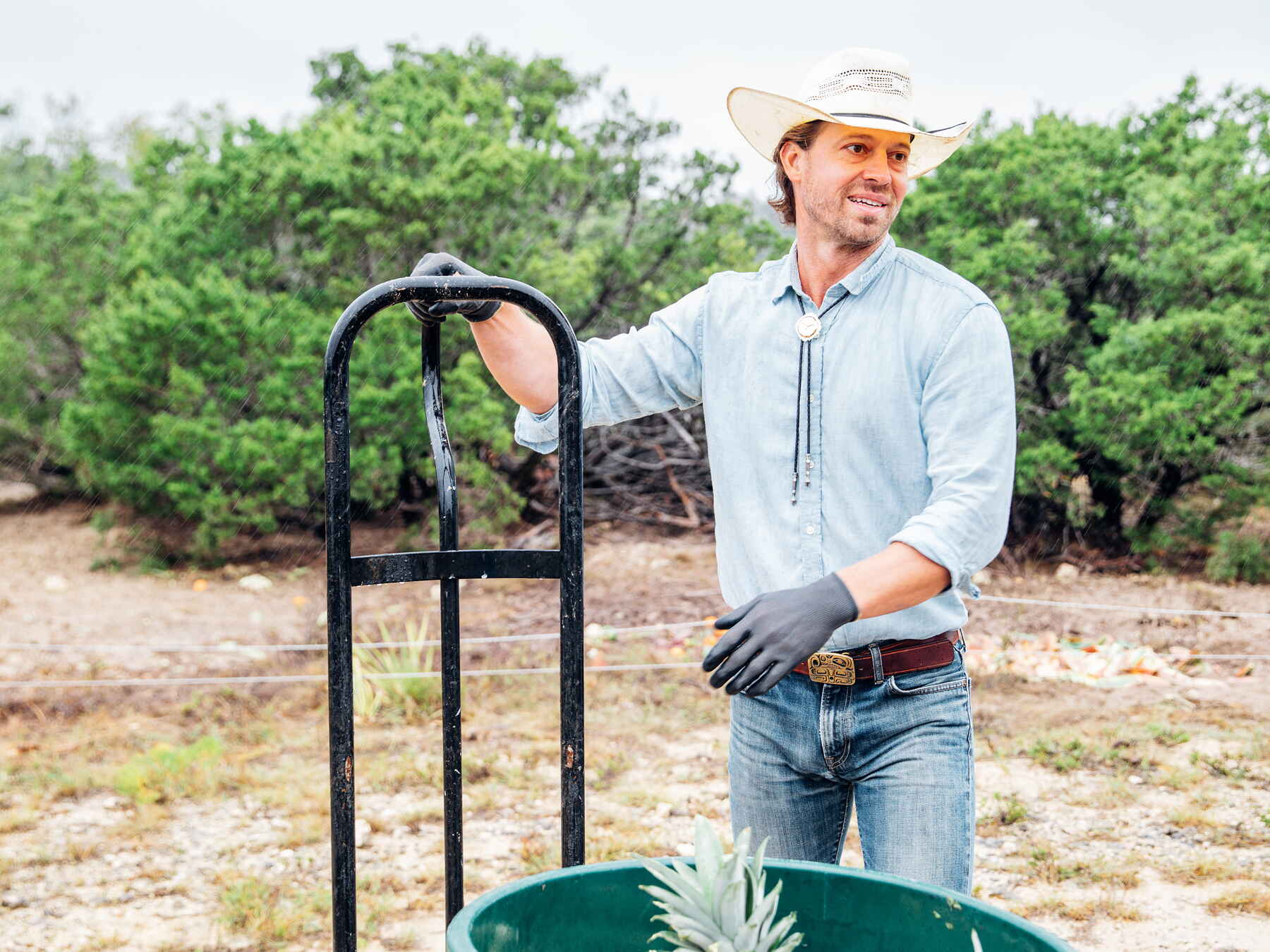 Farmer holding a shovel next to a Brute compost bin filled with plant scraps in an orchard