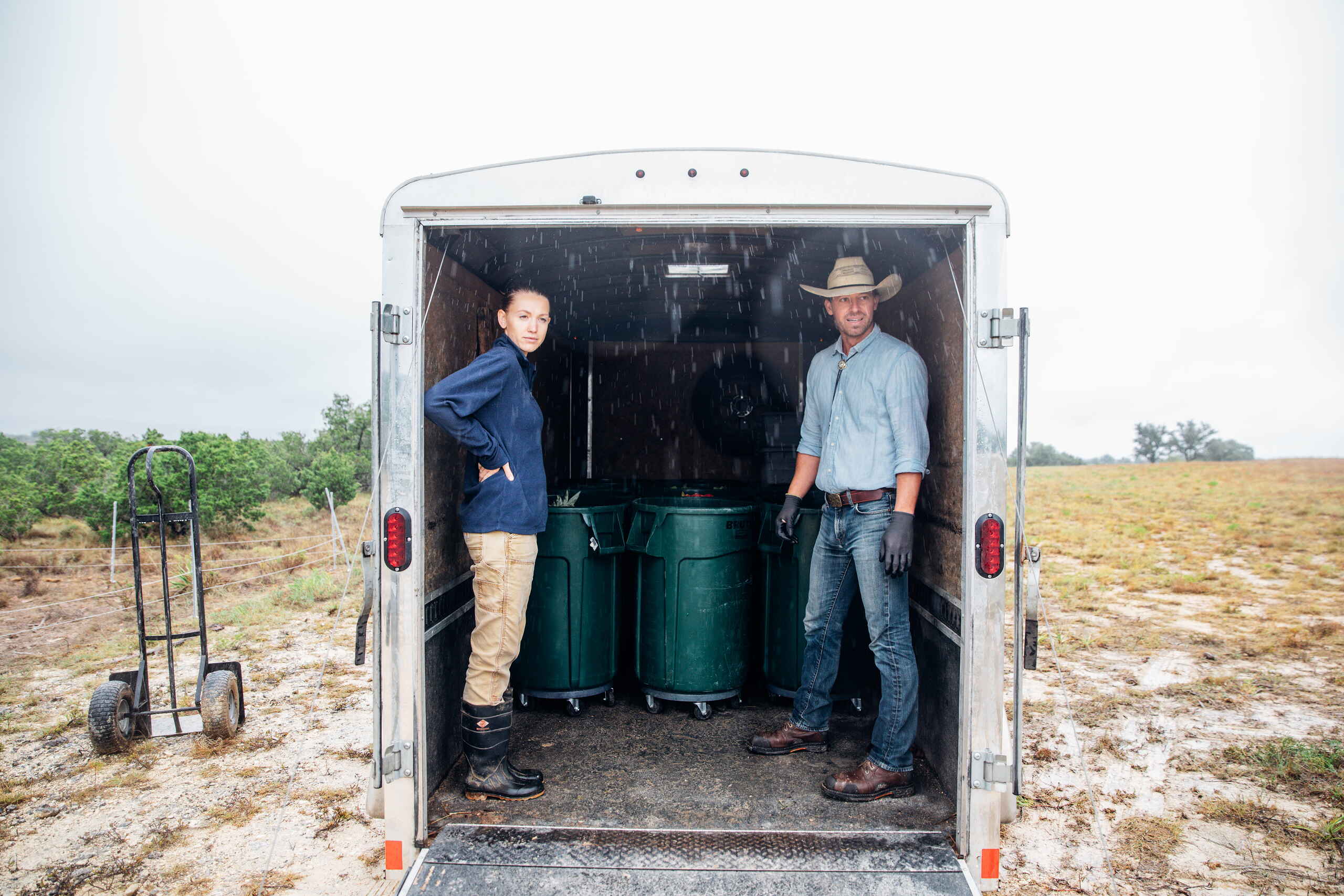 Tina and Orion Weldon stand inside a utility trailer displaying green water storage barrels on their ranch