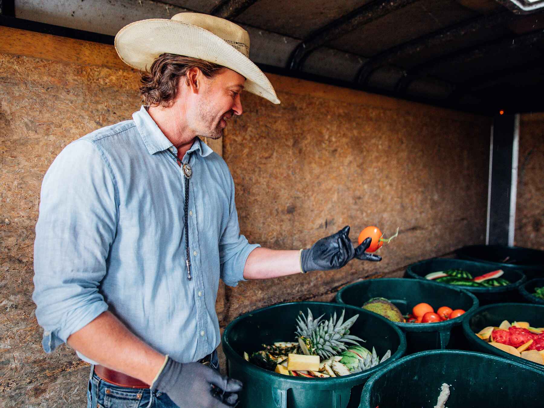 Farmer holding a fresh habanero pepper while standing beside bins of colorful produce at his farm stand