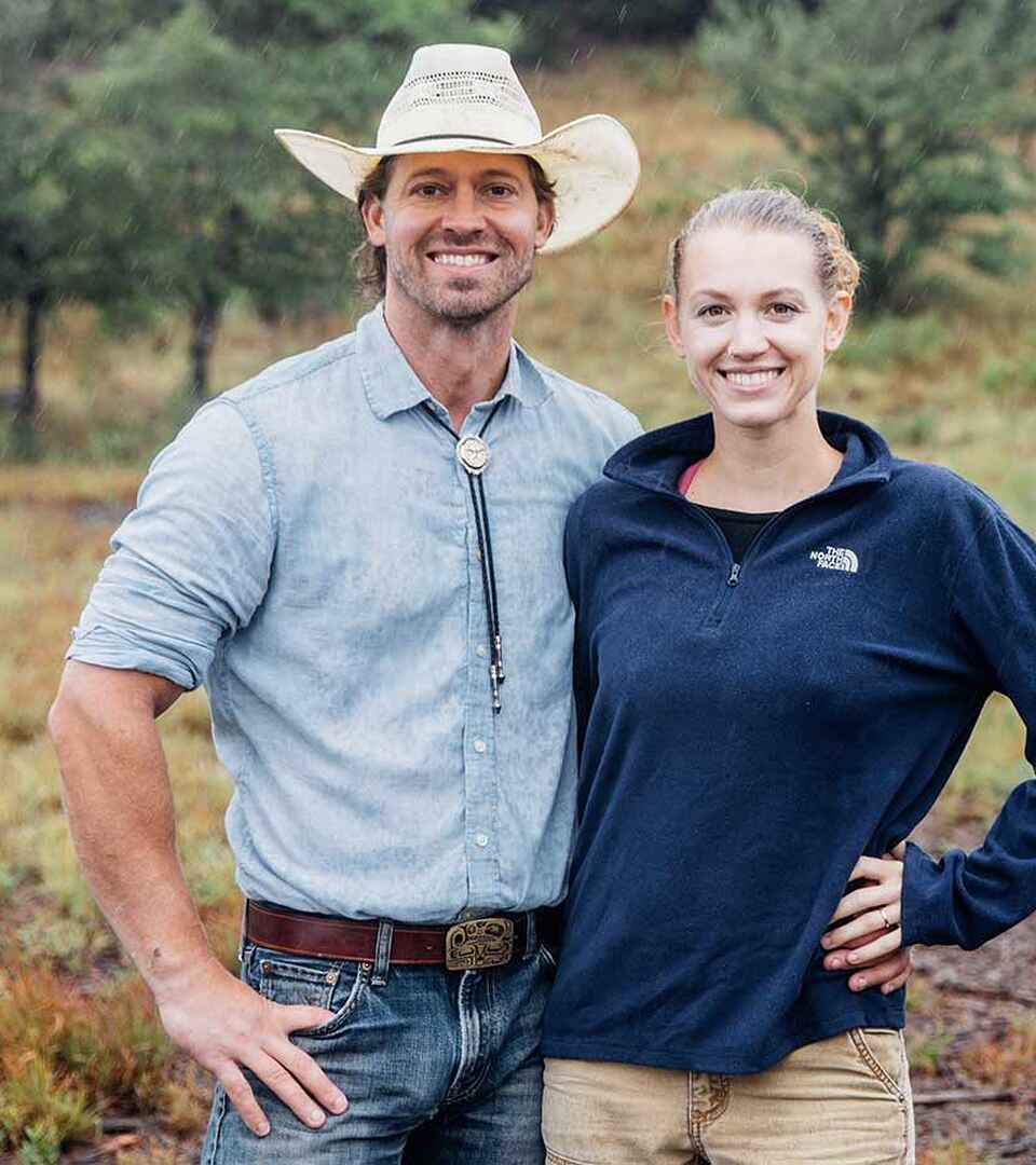 Tina and Orion Weldon smiling together outdoors with forested hills in the background