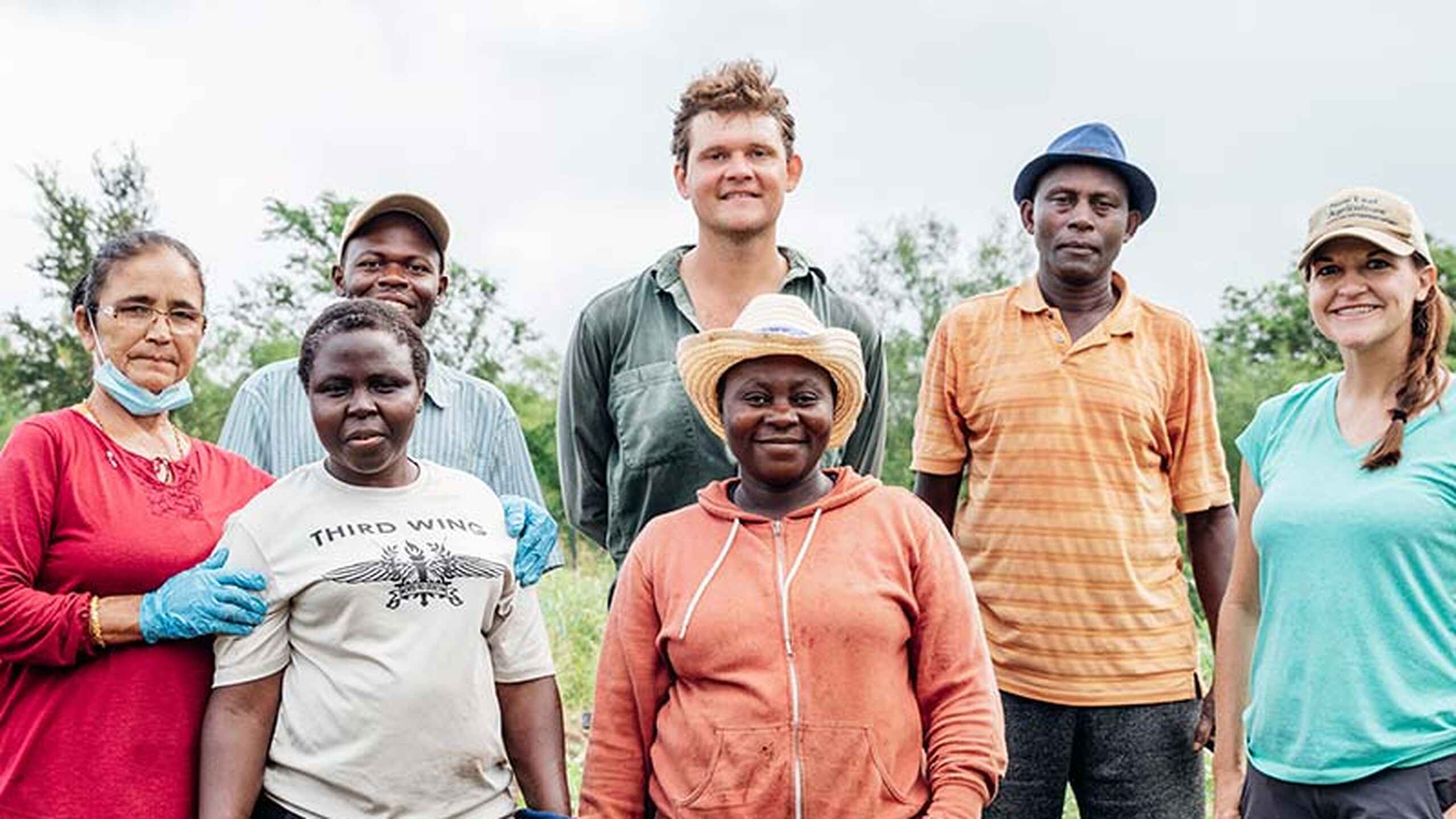 Wandaka Heritier Musungira stands with a diverse team of farmers and agricultural workers in a cultivated field