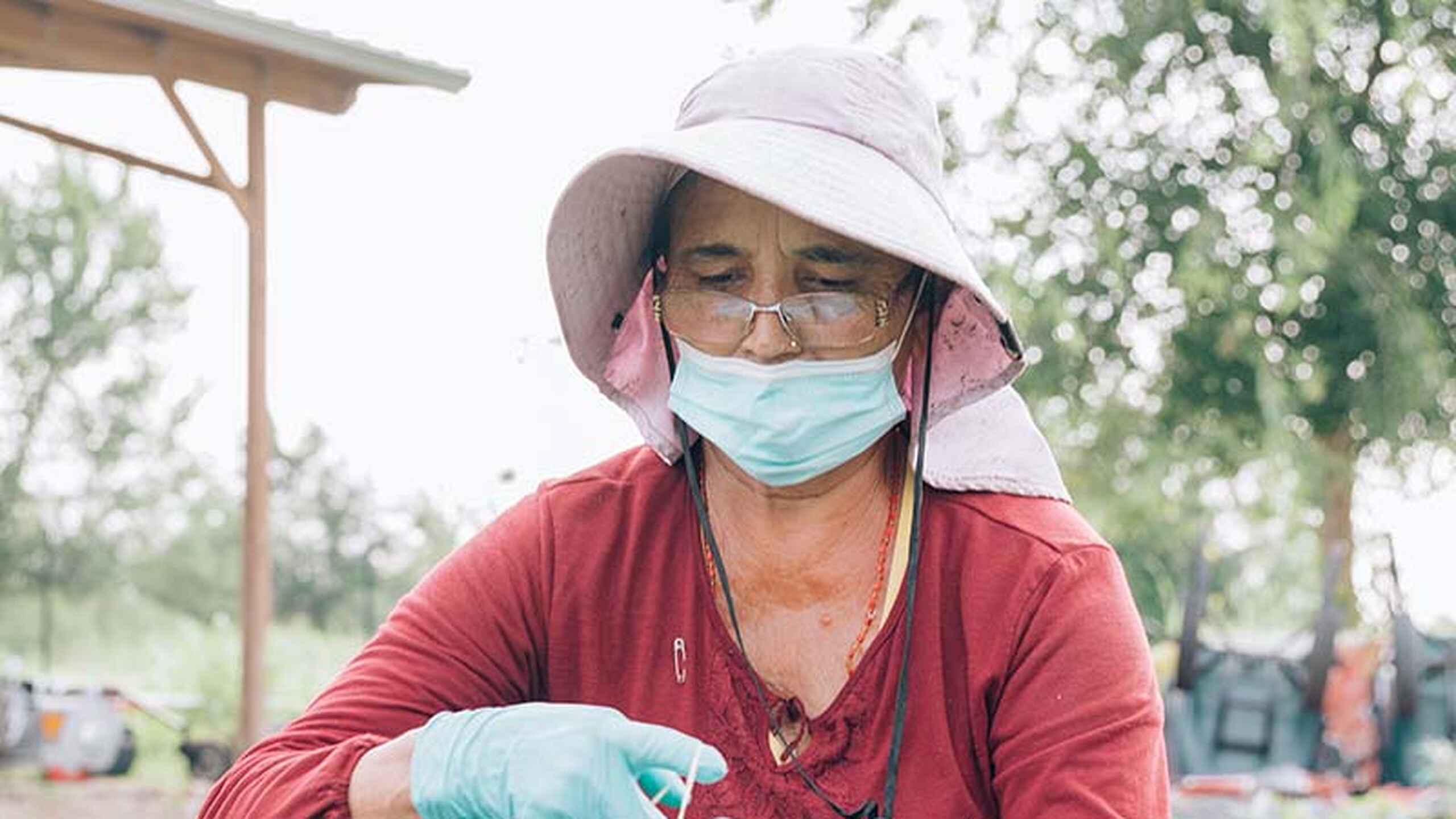 Wandaka Heritier Musungira tends to seedlings in a garden bed wearing protective gear and a wide-brimmed hat