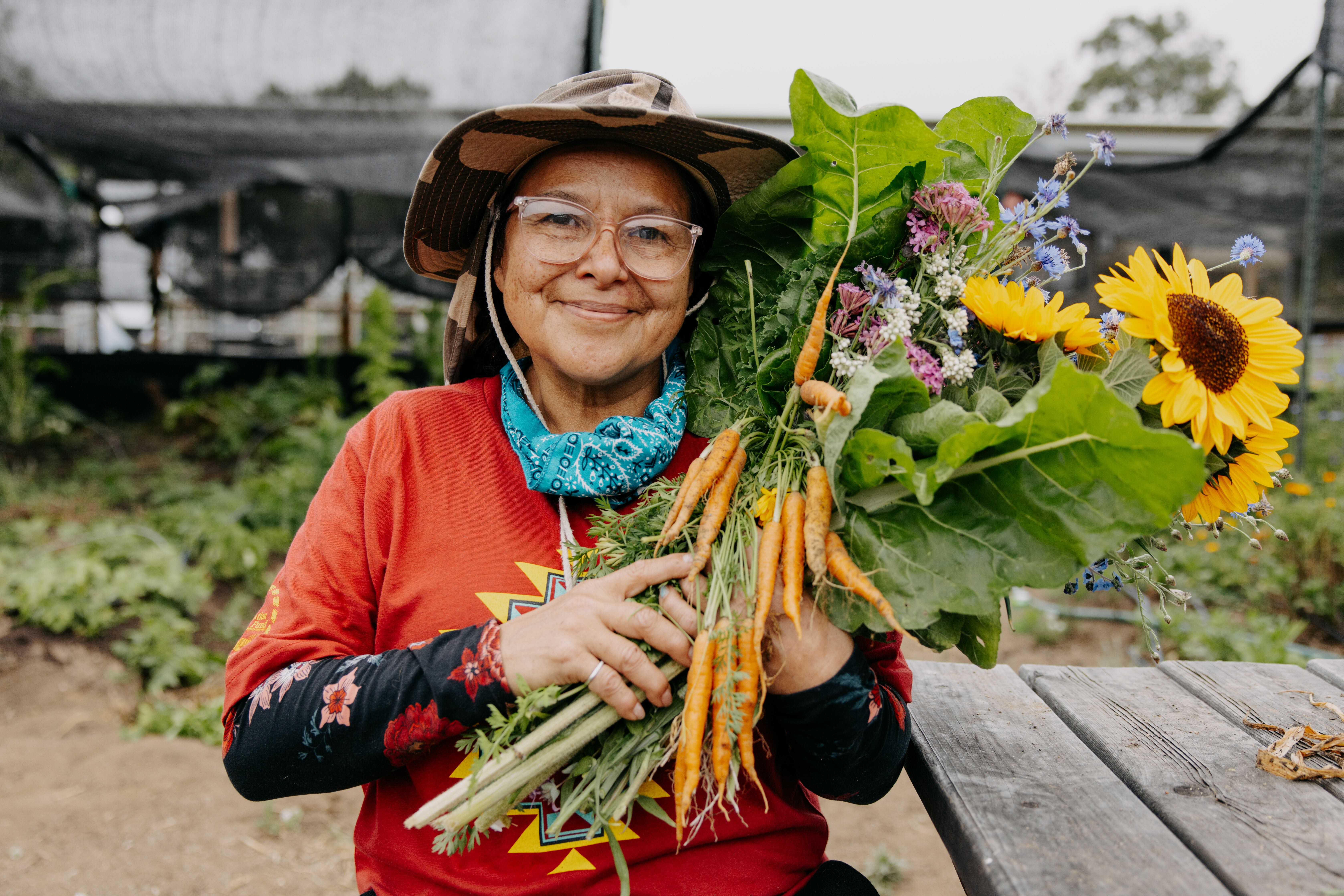 Woman holding harvested carrots and sunflowers in a greenhouse garden